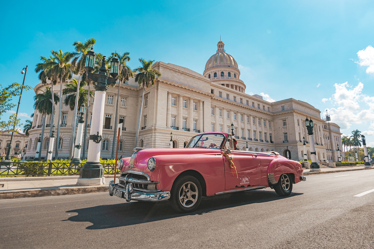 Old classic American pink car rides in front of the Capitol.