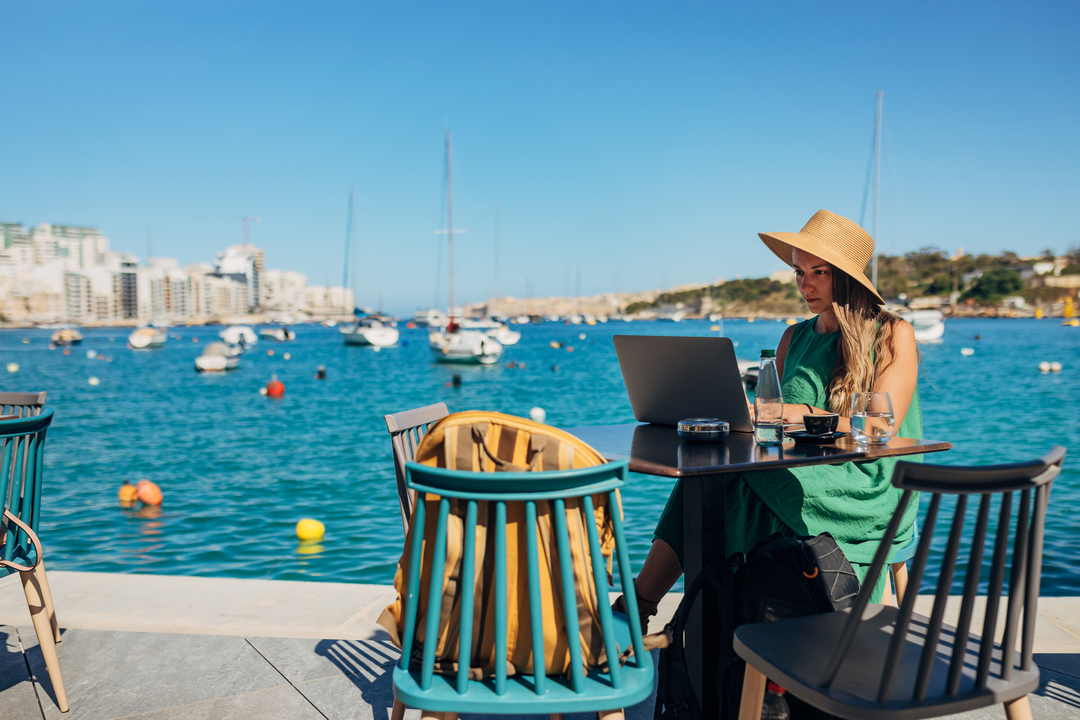 A business woman sitting in a coffee shop on the dock, not far from the sea and working on a laptop