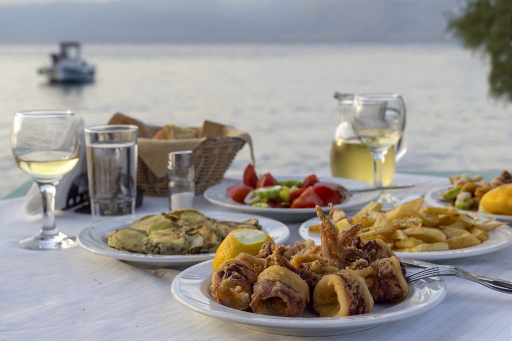 Dinner of fried squid, fried zucchini, french fries, salad and glasses with wine close-up