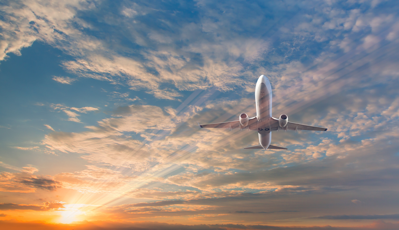 Airplane flying over tropical sea at sunset